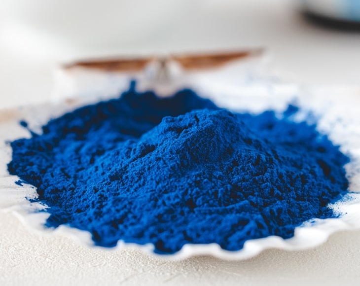 Łyżka z niebieską spiruliną na tle szklanki z wodą