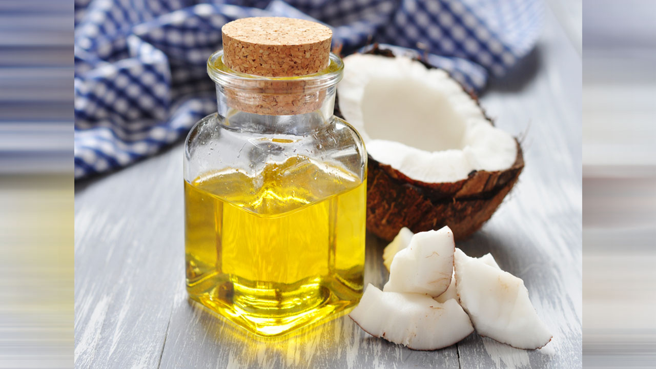 Kobieta wlewająca olej kokosowy z łyżką na rozgrzaną patelnię w jasnej kuchni